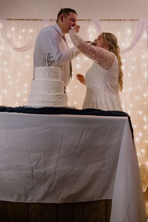 Bride and groom cutting their white wedding cake decorated with a custom topper, with fairy lights backdrop.
