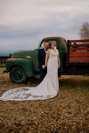 Bride and groom pose in front of a vintage green farm truck on their rustic outdoor wedding day.
