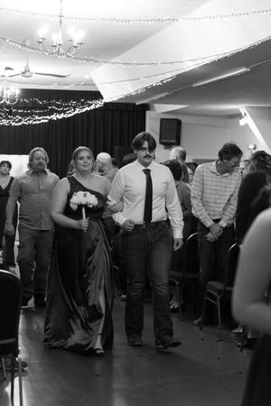 Black and white photo of a bridesmaid and groomsman walking down the aisle at a wedding ceremony.