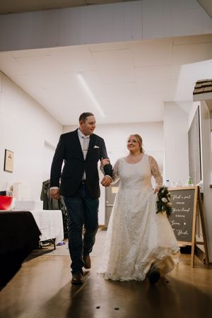 Bride in lace gown and groom in dark suit walk hand-in-hand at their wedding reception venue.
