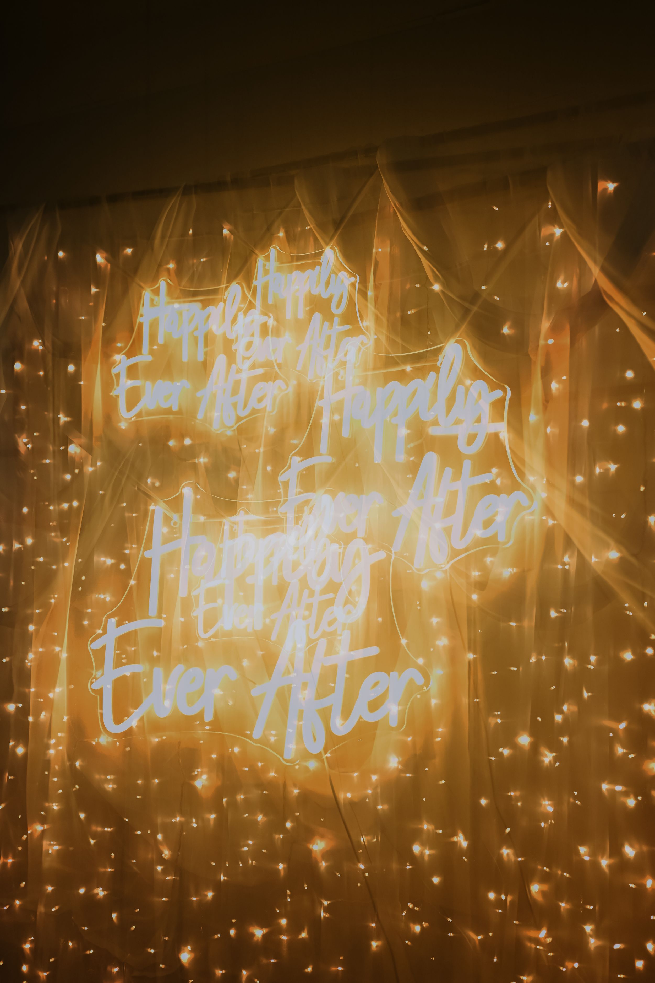 Neon sign reading Happily Ever After glowing against a sparkling fairy light backdrop at a wedding reception.