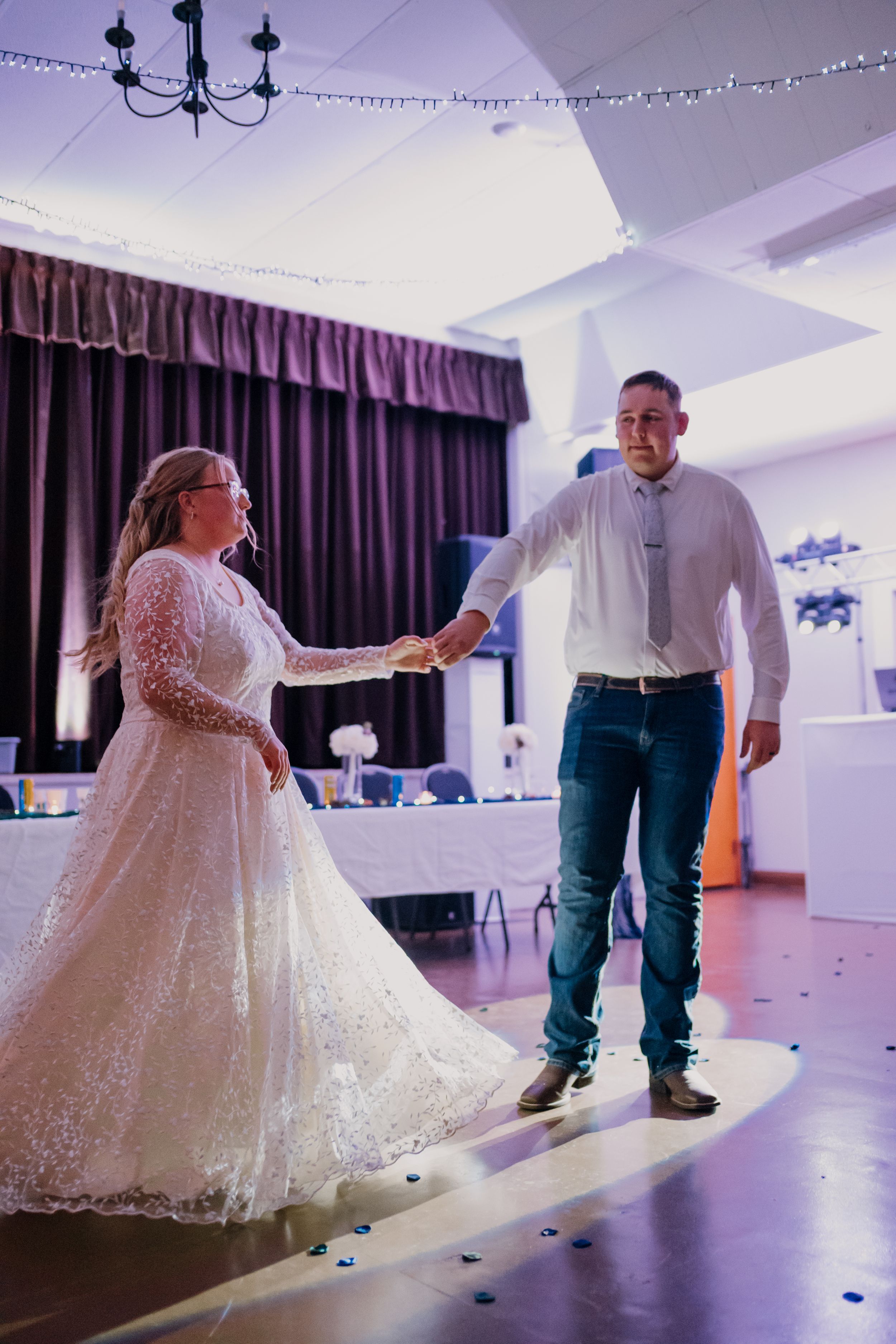 Bride and groom share their first dance in a decorated wedding reception hall, bride wearing a long lace gown.