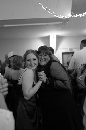 Two women smile and hold hands while dancing together at a formal event in black and white photo.