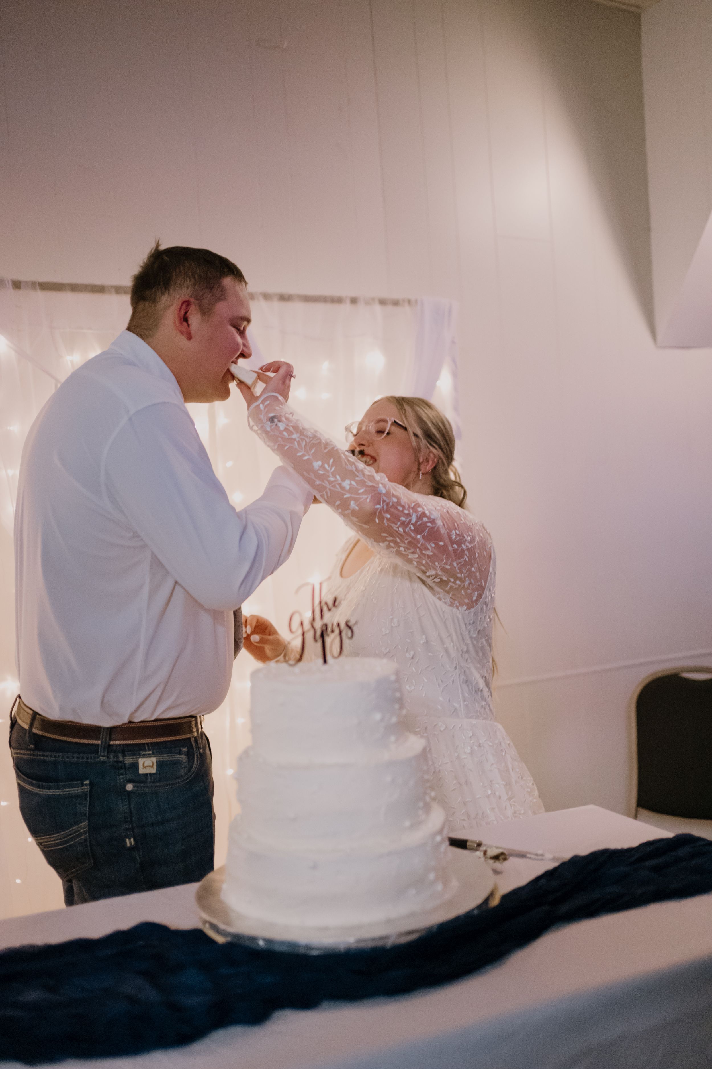 Bride and groom cutting their white four-tier wedding cake adorned with a gold cake topper at their reception.
