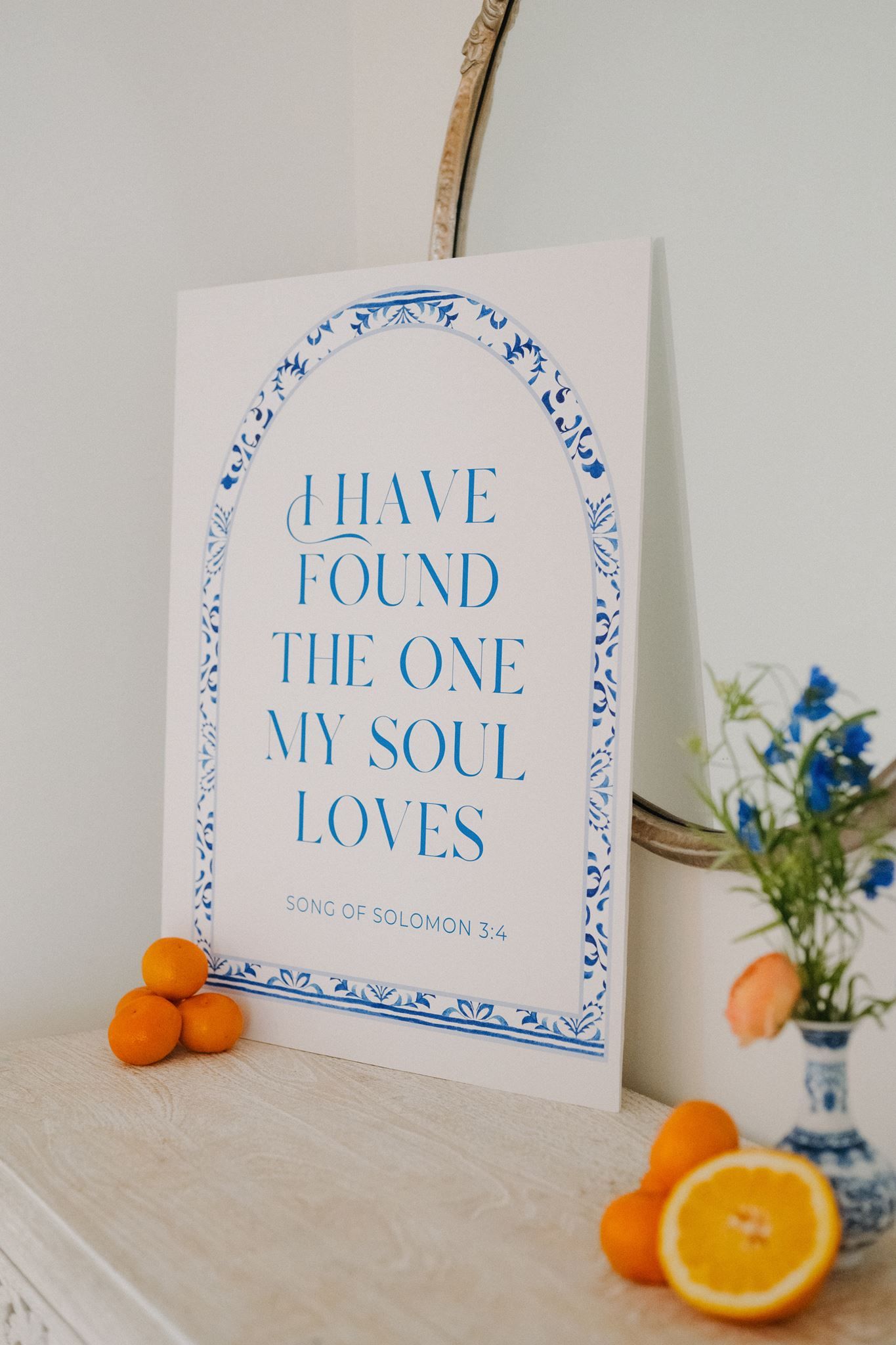 Blue and white arch print with Song of Solomon 3:4 quote, displayed on a shelf with fresh oranges and a floral vase.