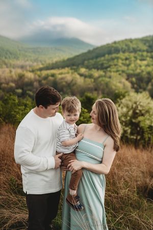 A family poses with their toddler son in a mountain meadow, mom in a sage green maternity dress.