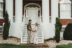 Couple holding hands on white staircase steps of a brick colonial mansion with tall columns.