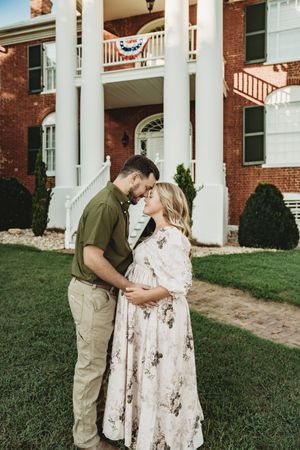 Couple sharing a tender moment in front of a historic brick mansion with white columns and patriotic bunting decorations.