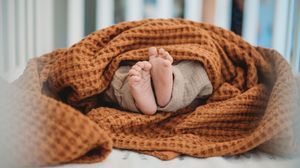 Tiny baby feet peeking out from a cozy orange waffle knit blanket in a white crib.