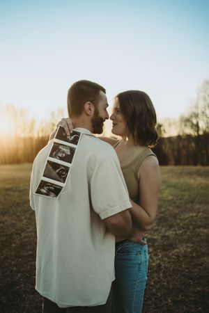 Couple sharing romantic moment holding ultrasound images at sunset in outdoor pregnancy reveal photo.