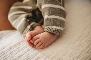Close-up of adorable baby feet in a striped knit onesie resting on a soft white blanket.