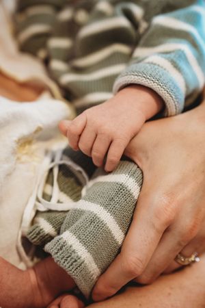Close-up of a newborn baby's tiny hand resting on an adult's hand, both wearing striped knit clothing.
