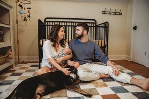 Couple sitting on floor with dog in nursery room, smiling at each other near black crib.