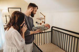 Parents admiring their newborn baby in a nursery crib, with a mobile hanging above in a cozy home setting.