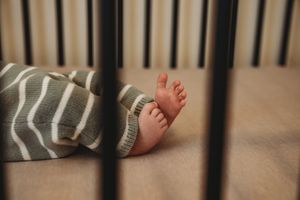 Close-up of newborn baby feet peeking out from a striped blanket inside a wooden crib.