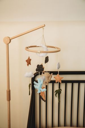 A wooden baby crib mobile with felt stars, clouds, and animals hanging above a dark wooden crib.