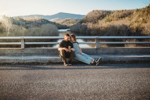 Couple sitting together on a bridge road with scenic mountain lake views in golden hour light.