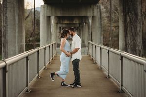 Couple sharing a romantic moment on a pedestrian bridge with concrete pillars in the background.
