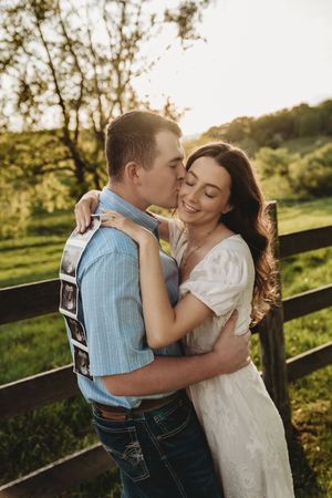 Couple sharing a romantic kiss outdoors at golden hour, man holding ultrasound images.