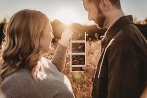Couple sharing a joyful moment outdoors at sunset, holding ultrasound photos to announce their pregnancy.