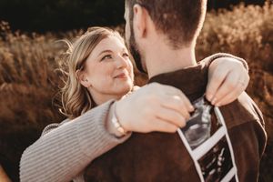 Couple embracing outdoors holding ultrasound photo, woman smiling warmly, golden field background, pregnancy announcement.