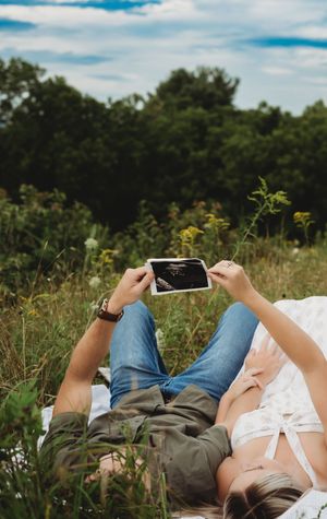 Couple lying in a meadow holding an ultrasound photo outdoors.
