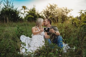 Couple kissing in a field holding an ultrasound photo at sunset.