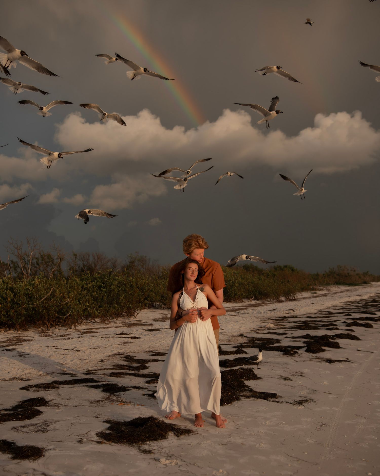 a sunlit romantic beach couple portrait beneath a rainbow, storm clouds and soaring seabirds along Florida's Gulf Coast.