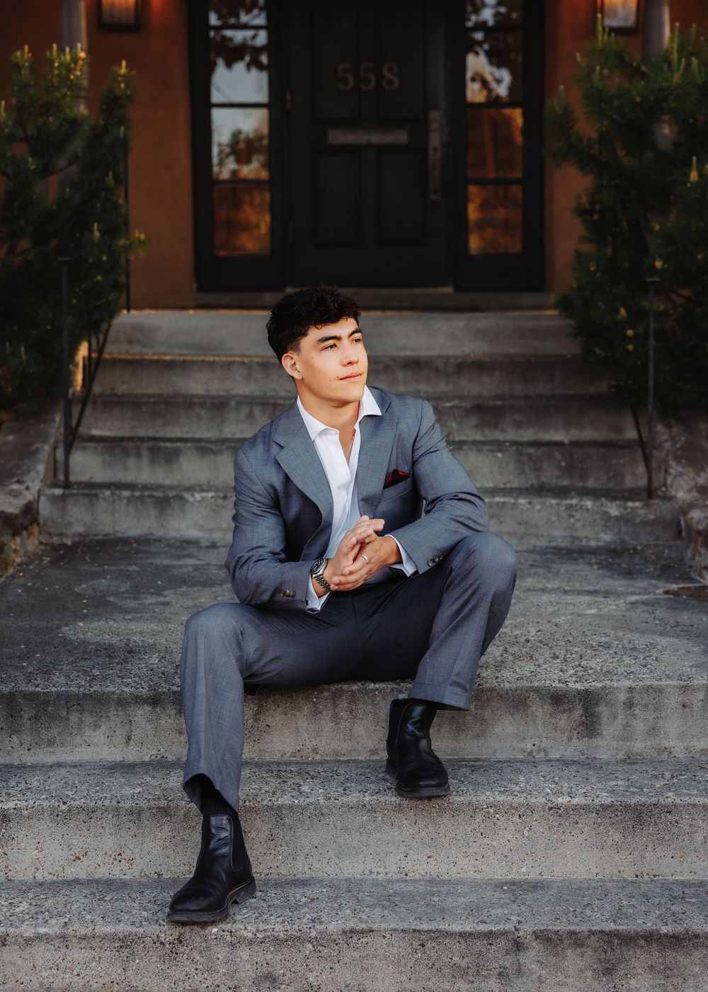 Young man in gray suit sitting on stone steps outside a building numbered 558.