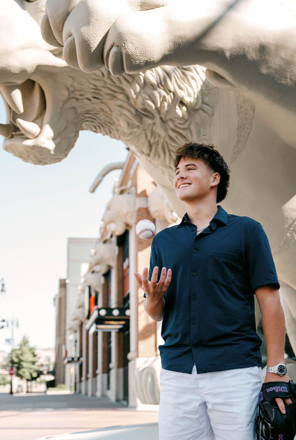 Smiling young man in navy shirt posing near a large tiger sculpture outside Comerica Park.