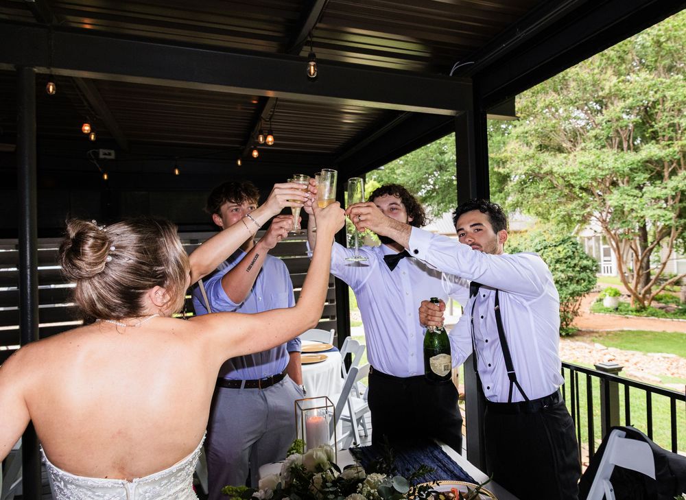 Wedding party toasting with champagne glasses under a covered outdoor venue during a reception celebration.
