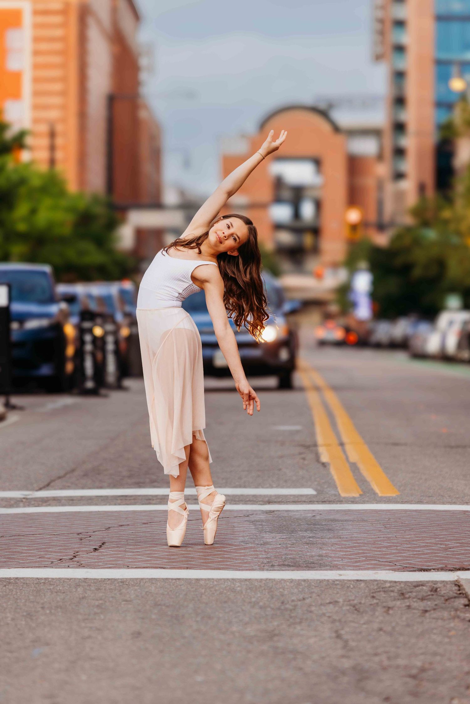 Graceful ballerina in white dress and pointe shoes dancing on an urban city street.