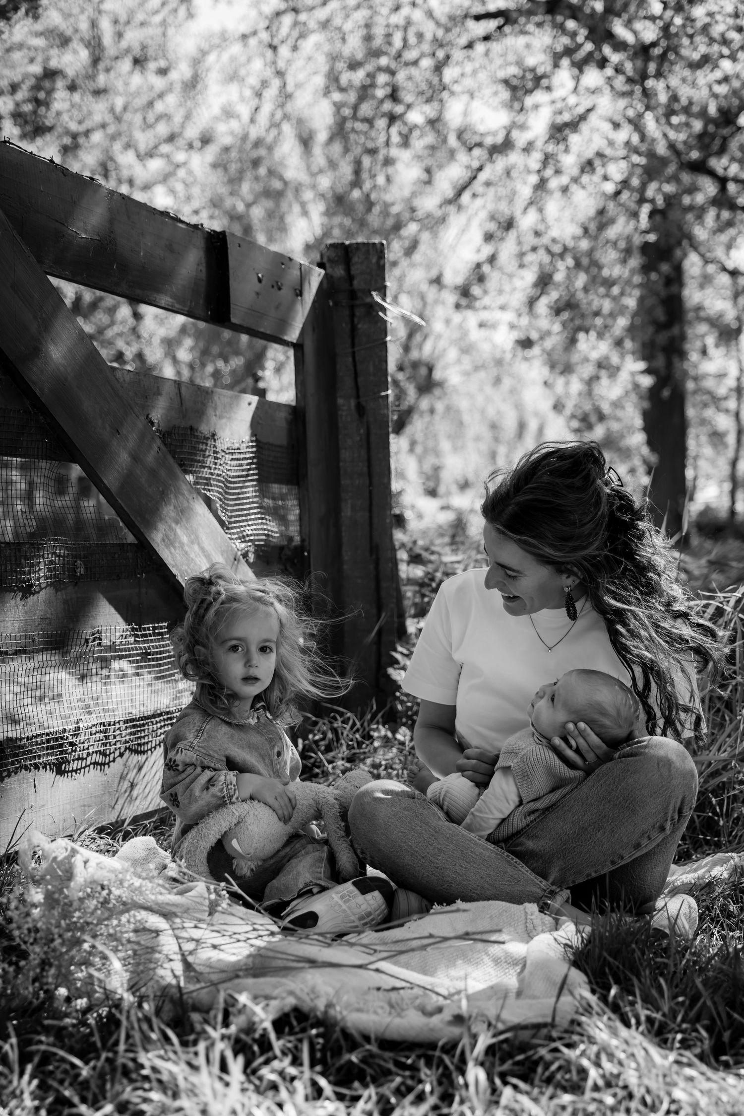 Black and white photo of a mother breastfeeding a newborn while sitting outdoors with her toddler daughter.