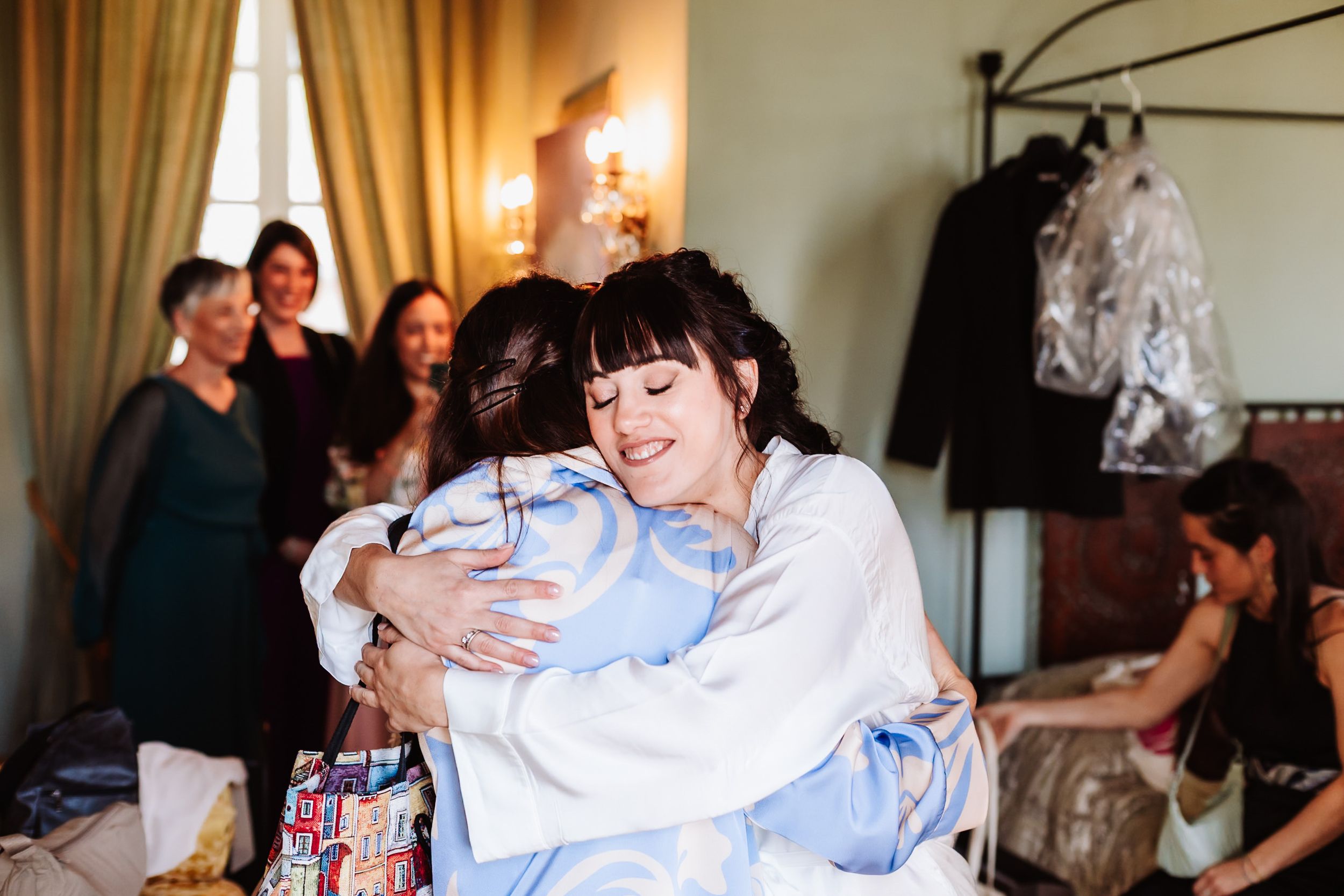 Two women sharing a warm embrace during wedding preparations in an elegantly decorated room.