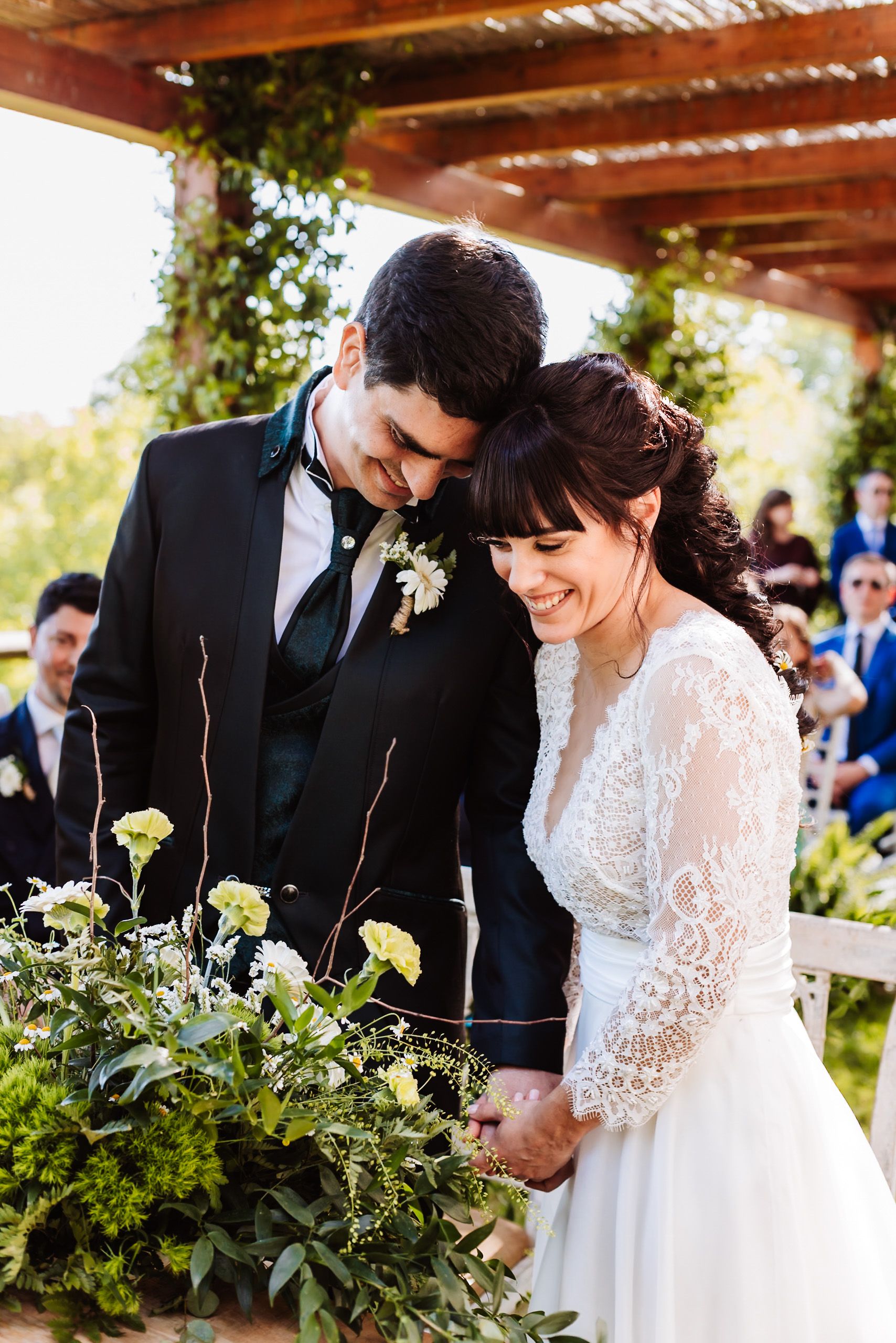 Bride and groom share an intimate moment at outdoor wedding ceremony, surrounded by lush greenery and white flowers.