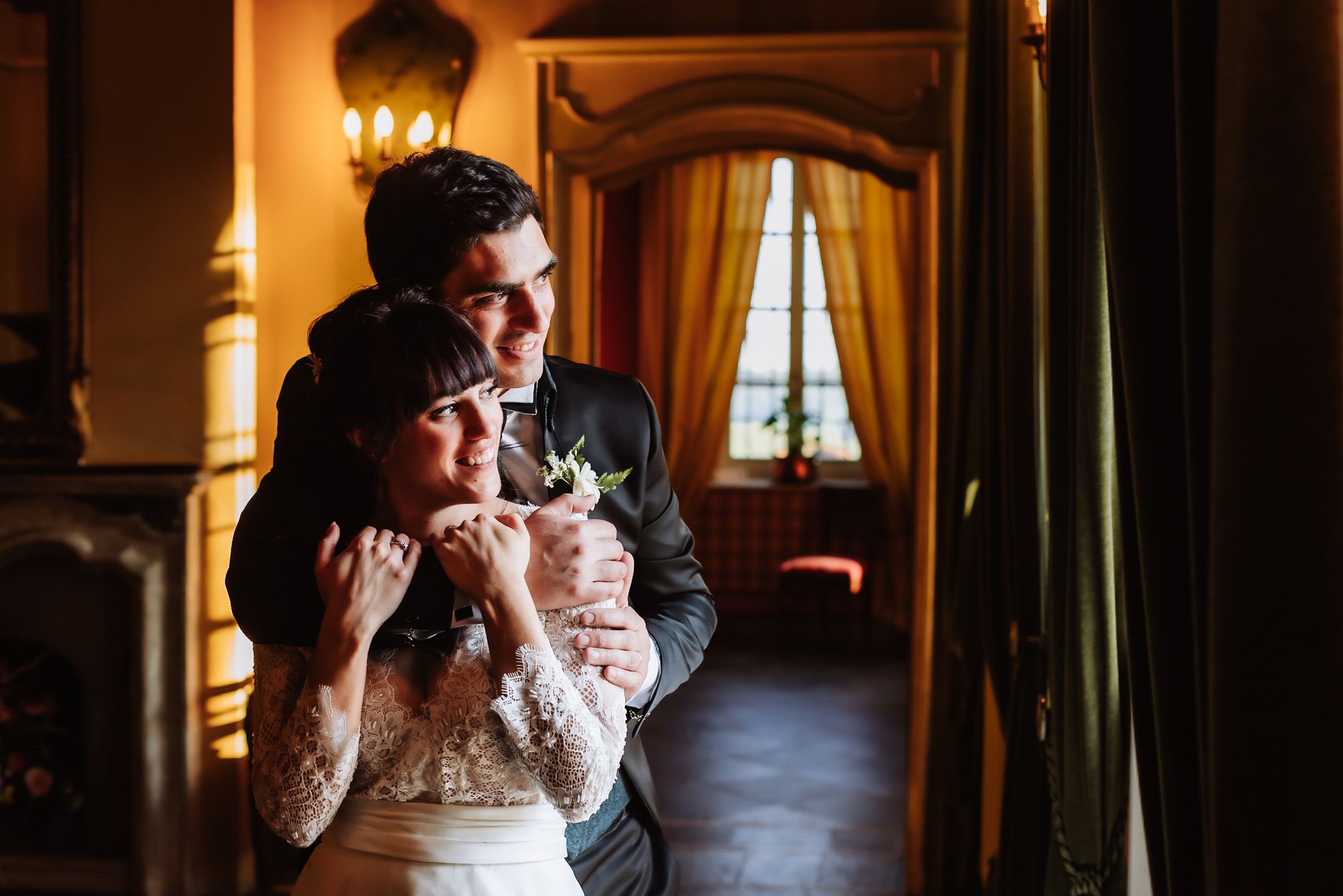 Bride and groom share a tender embrace in an elegantly lit room with golden curtains on their wedding day.
