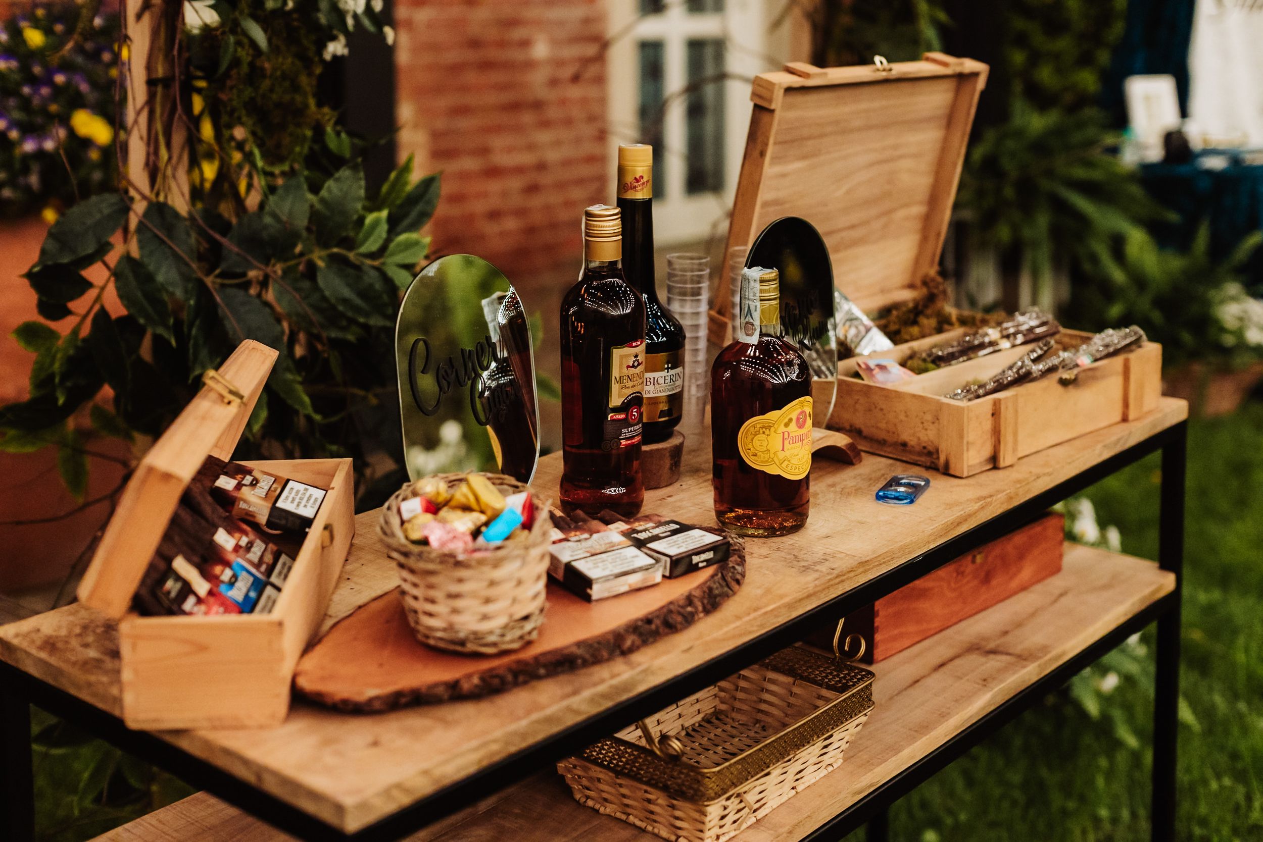 Rustic wooden table display with liquor bottles, wicker baskets, and wooden boxes at an outdoor event.