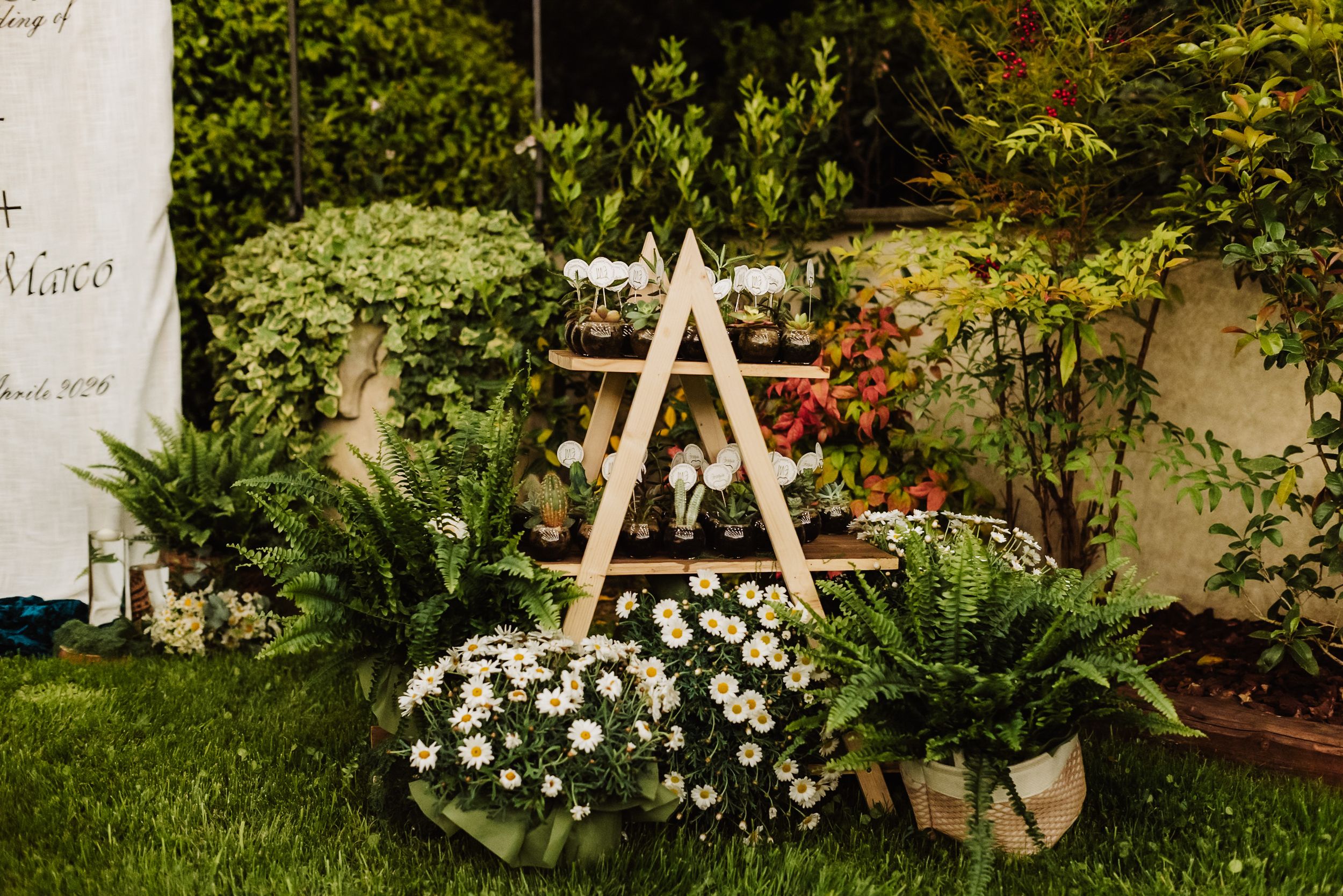 Wooden A-frame tiered plant stand adorned with daisies and lush greenery in a garden setting.