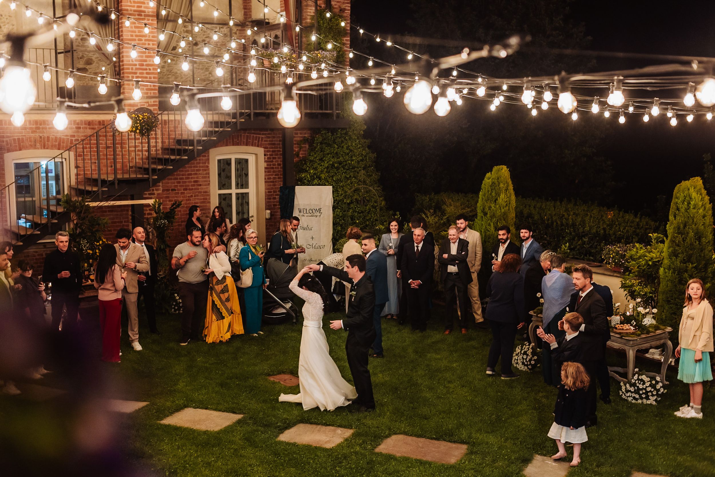 Bride and groom share first dance under string lights at elegant outdoor evening wedding reception.