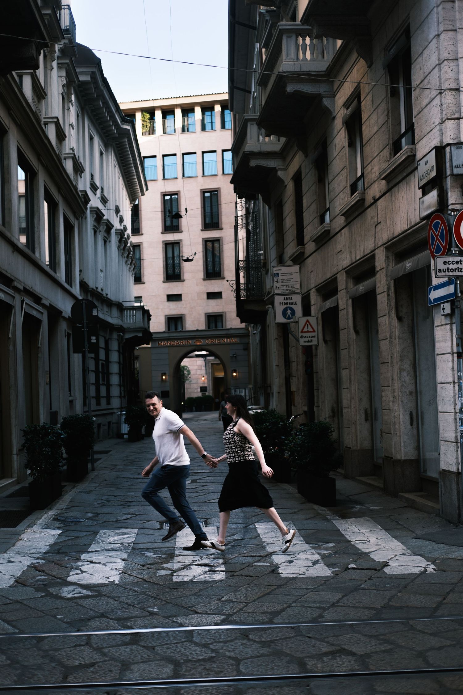 Couple holding hands crossing a cobblestone street in a European city alley with classic architecture.