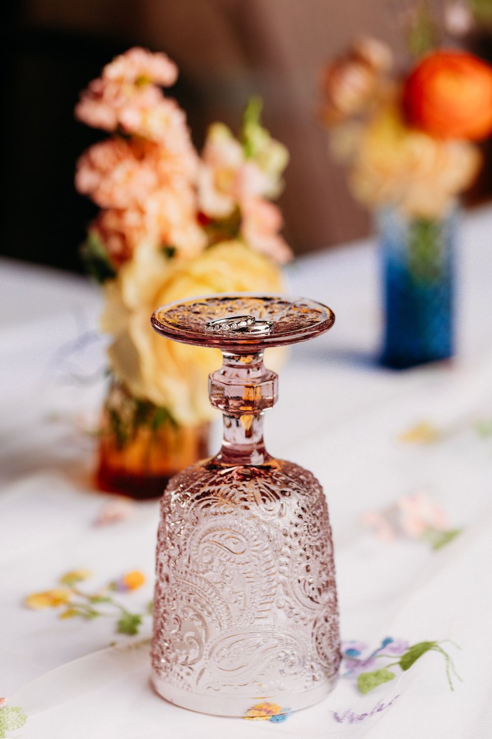 Ornate crystal wine glass turned upside down on floral tablecloth with colorful flower arrangements in background.