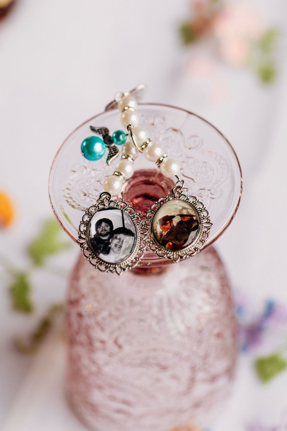 Vintage silver locket charms with black and white photos, pearl beads, and teal accent on a pink glass.