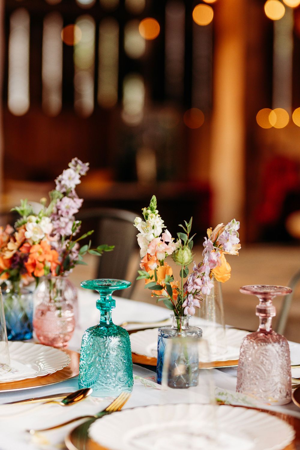 Elegant wedding reception table with colorful glassware and fresh floral arrangements.