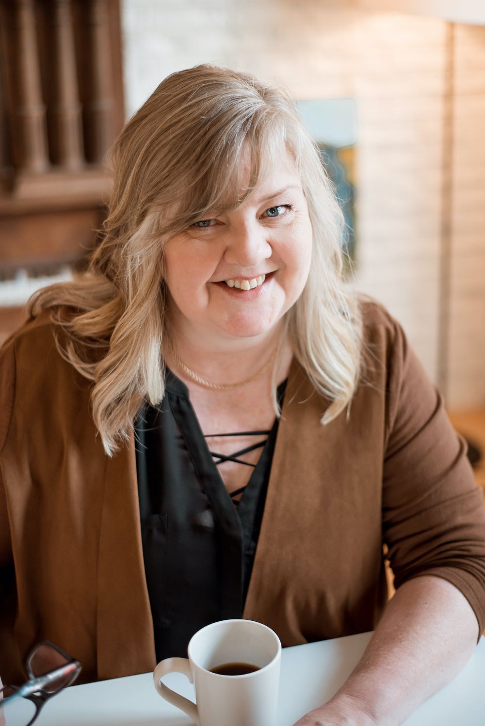 Person enjoying coffee while seated at table wearing brown blazer.