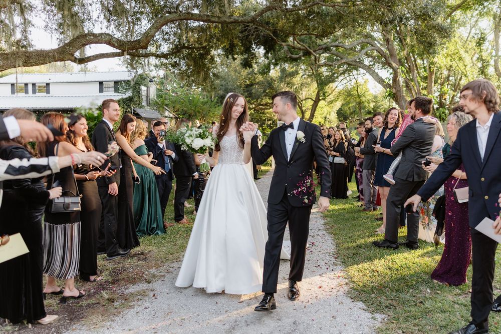 Bride and groom walk joyfully through cheering guests at an elegant outdoor wedding ceremony.