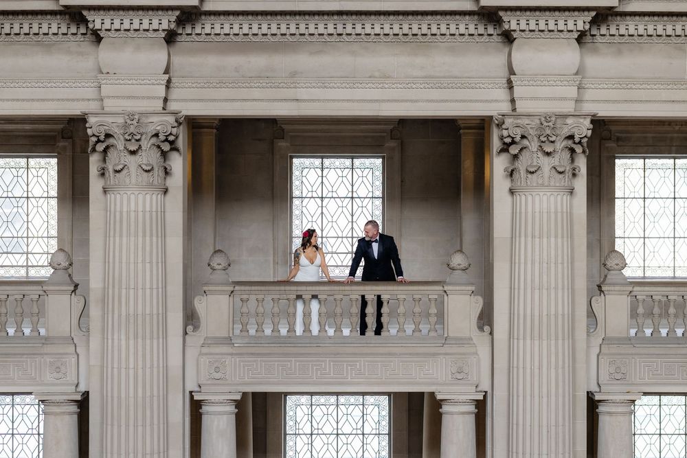 Bride and groom standing on elegant balcony with tall white columns at a grand wedding venue.