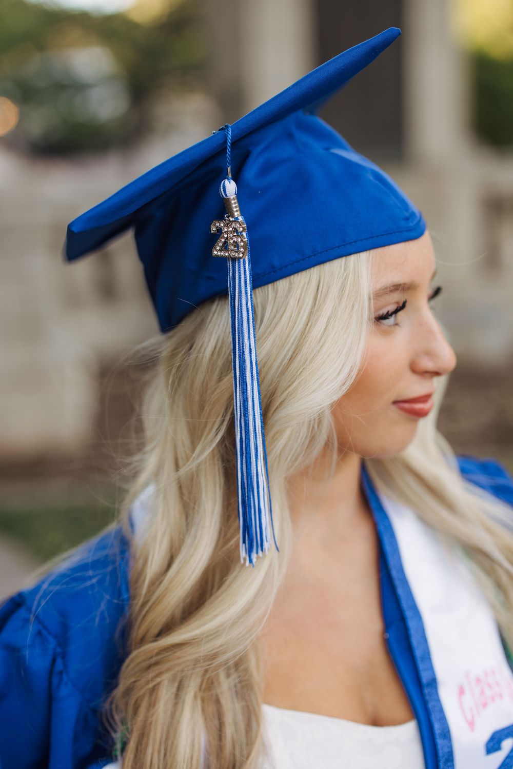 Close-up profile of blonde graduate wearing a royal blue cap with tassel and graduation robe.