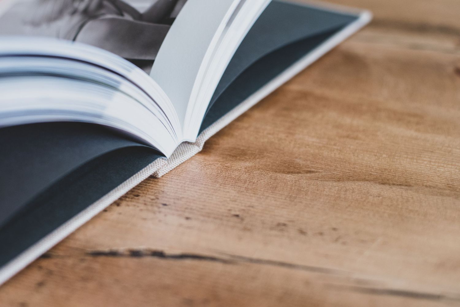 Open magazine or photo book lying flat on a rustic wooden table, showcasing glossy pages in soft natural light.