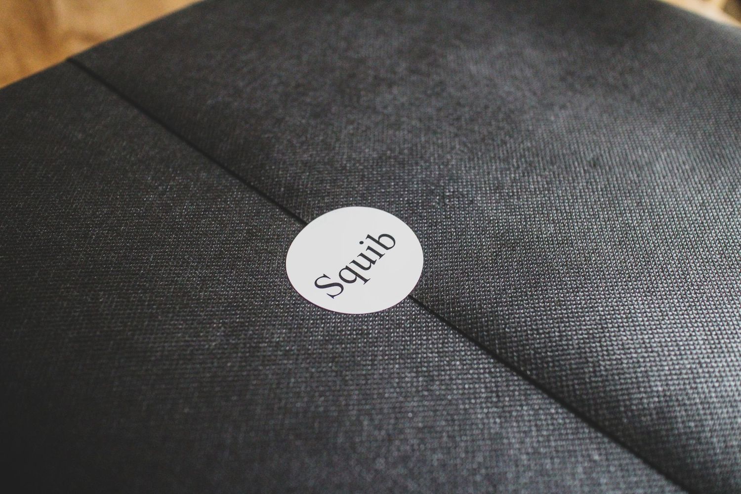 Close-up of a dark charcoal fabric box with a small white circular Squib brand sticker on top.