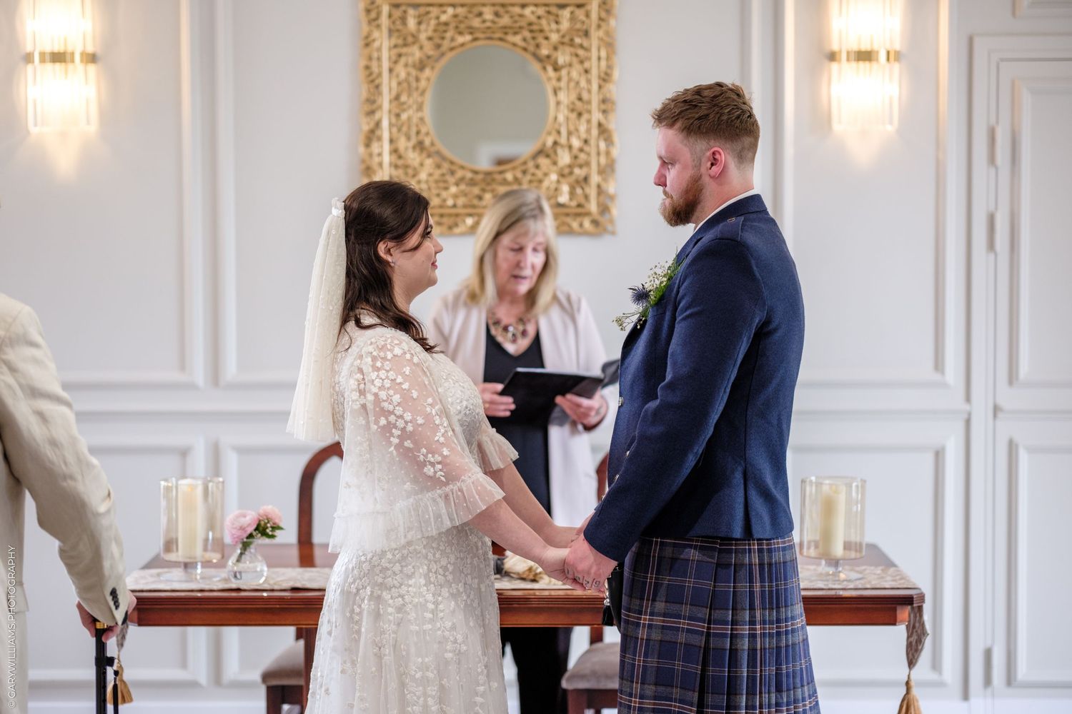 Couple exchanging vows at elegant wedding ceremony with officiant, candles, and gold mirror backdrop.